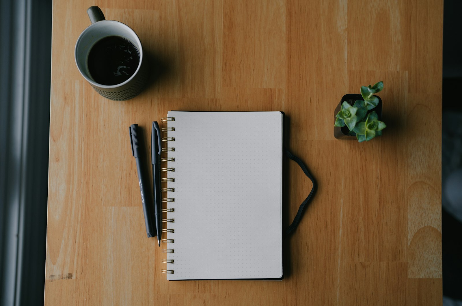 Carnet, stylos et tasse posés sur un bureau en bois, pour préparer le budget d'une formation