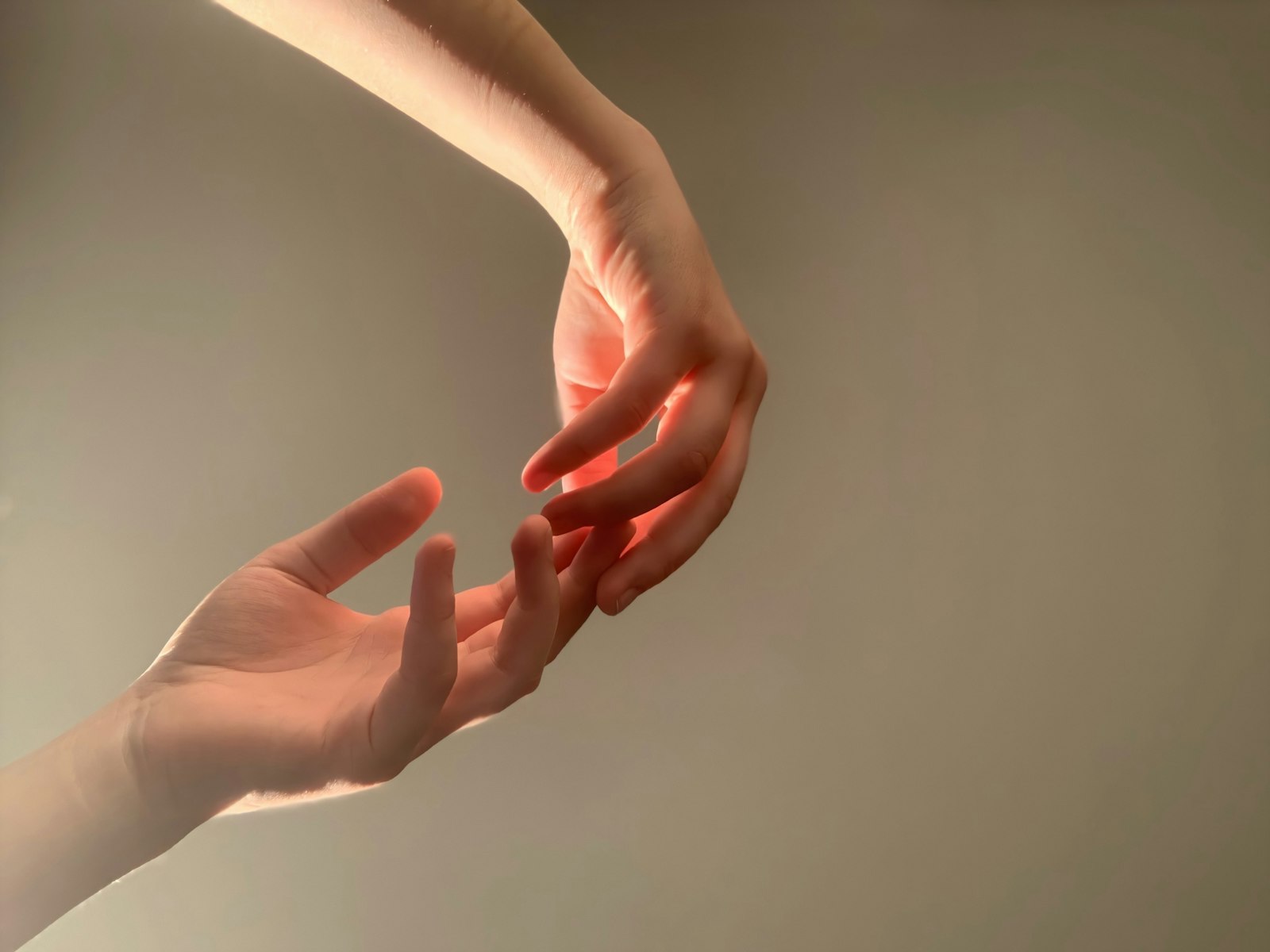 Deux mains qui se frôlent du bout des doigts, éclairées par une lumière douce, sur un fond neutre