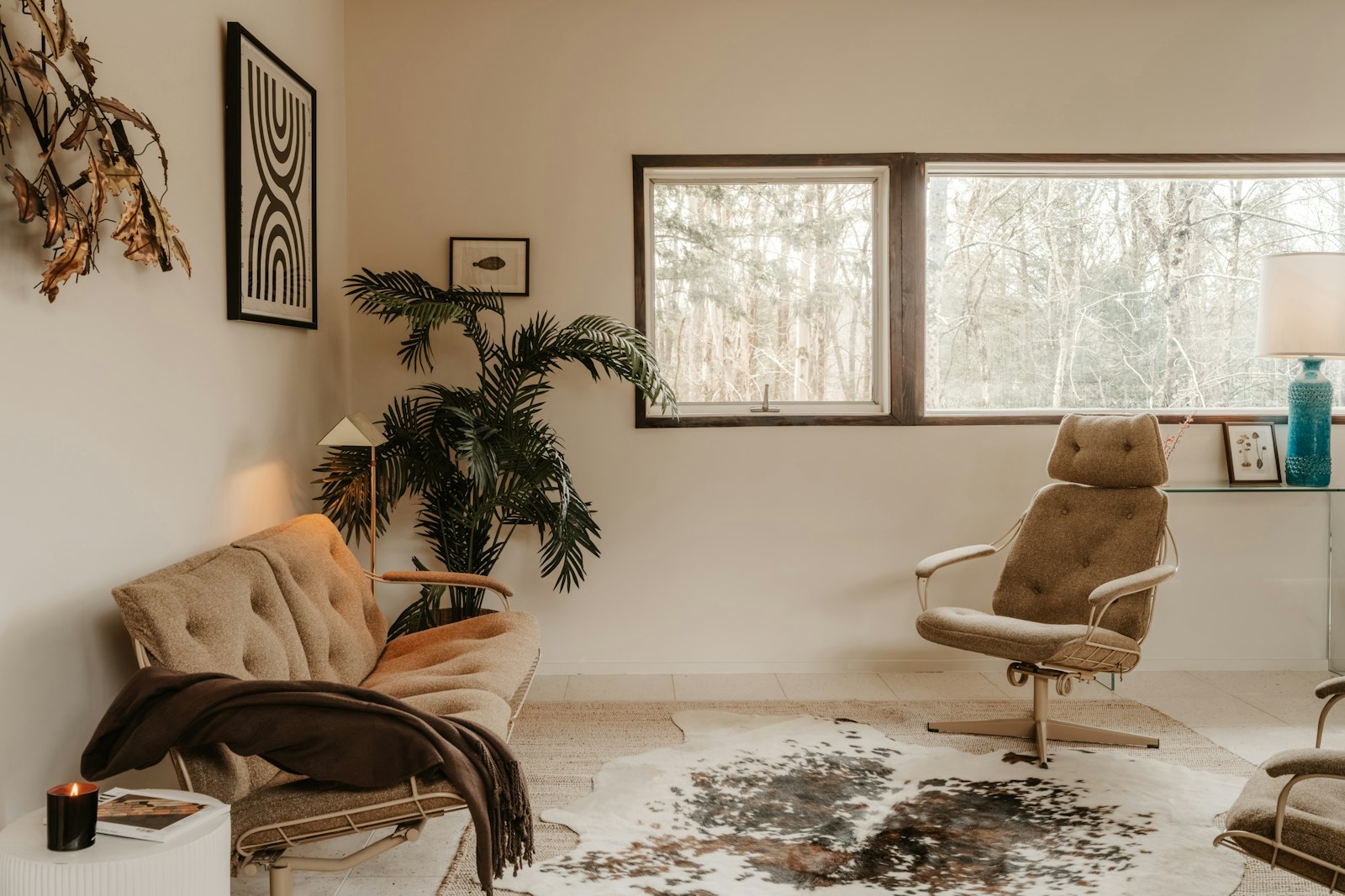 Un salon lumineux et calme avec un canapé, un fauteuil, une grande plante et une bougie près de la fenêtre