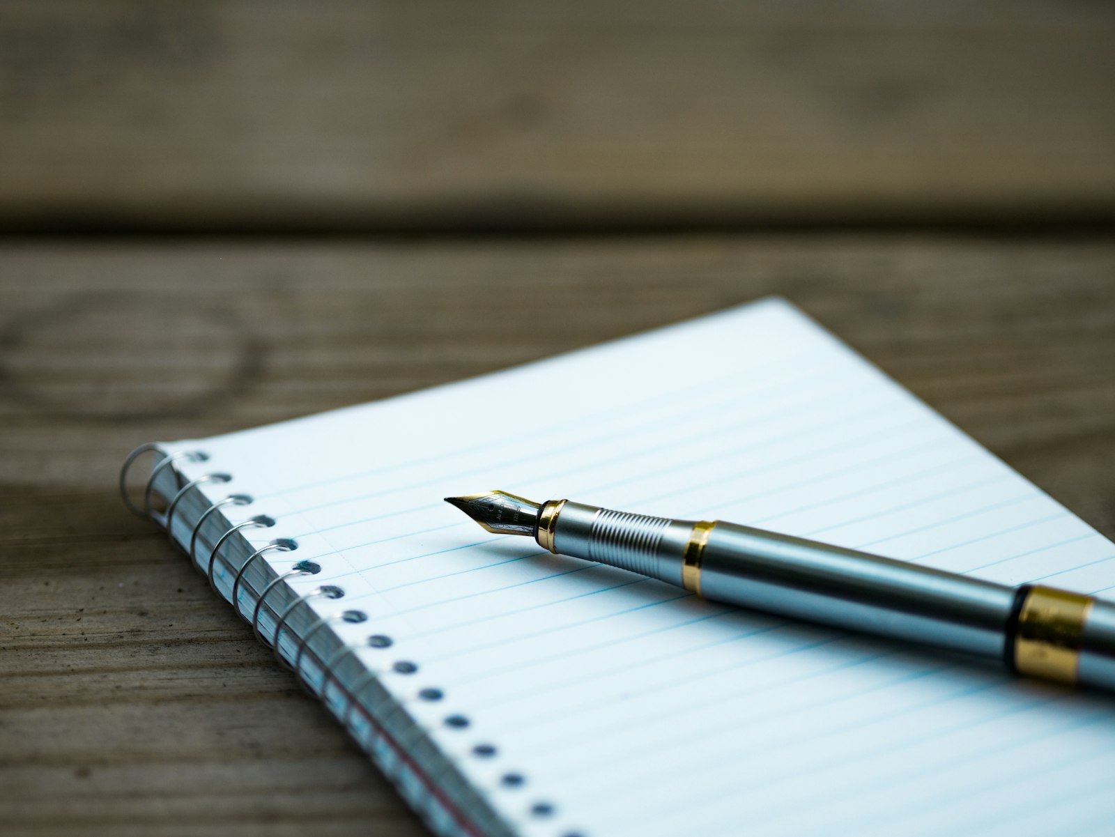 Un carnet à spirale et un stylo plume posés sur un bureau en bois, prêts pour prendre des notes