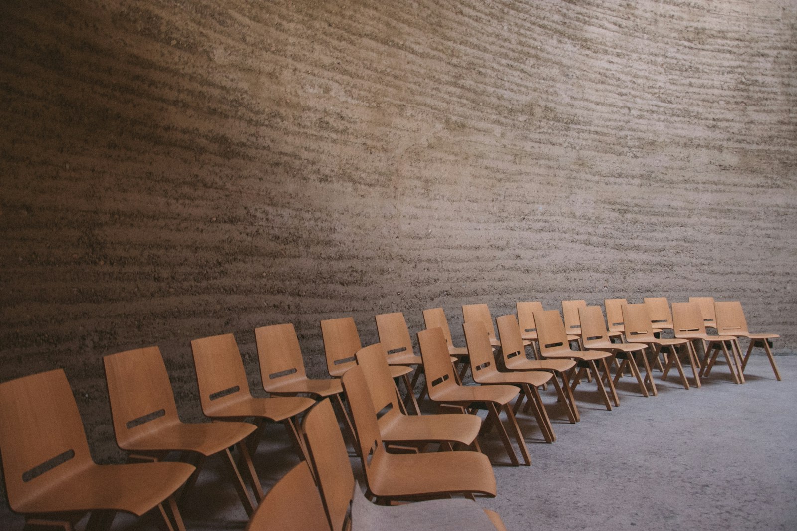 Des rangées de chaises en bois vides alignées dans une grande salle au mur de pierre brute