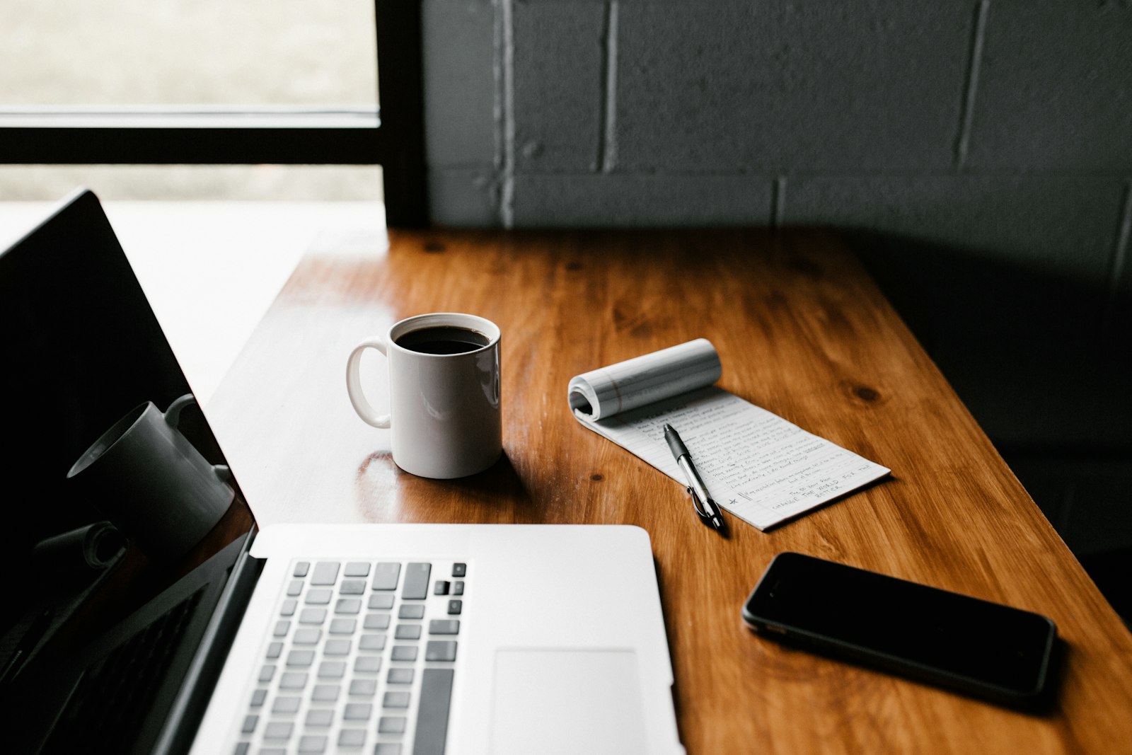 Un bureau en bois avec un ordinateur portable, une tasse de café, un bloc-notes et un téléphone