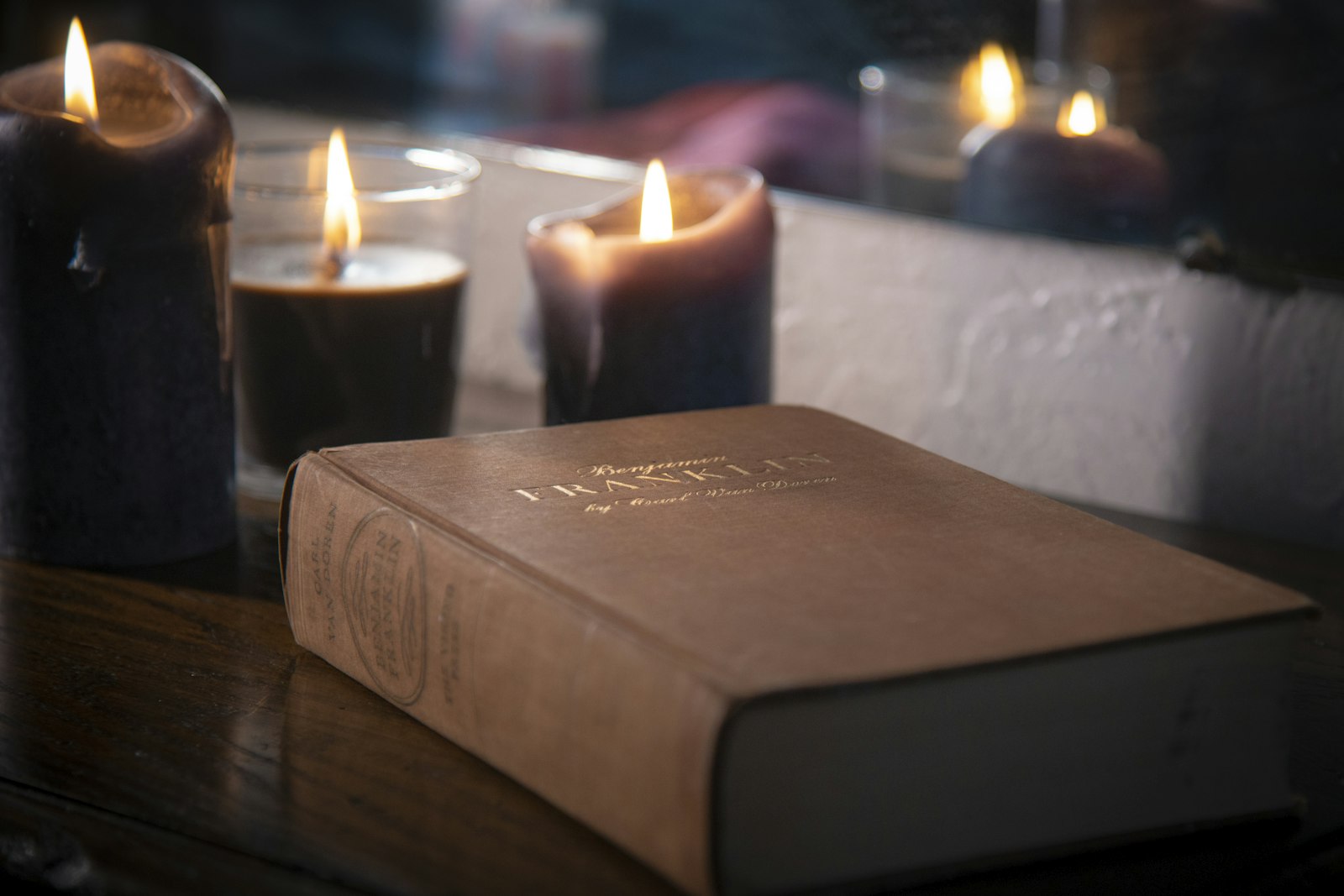 Gros livre relié posé sur une table en bois, à la lueur de plusieurs bougies allumées