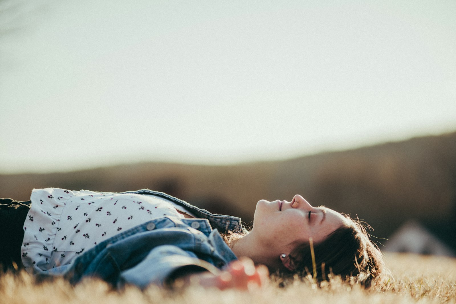 Une jeune femme allongée dans l'herbe sèche, les yeux fermés, le visage tourné vers le ciel à la lumière du soir