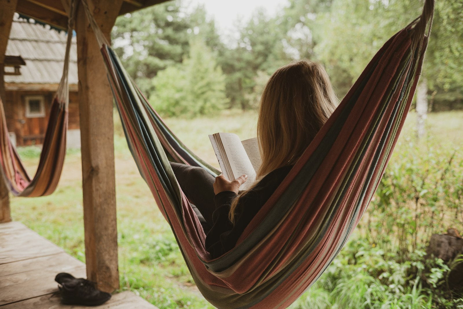 Une personne lit dans un hamac entre deux arbres, dans la nature