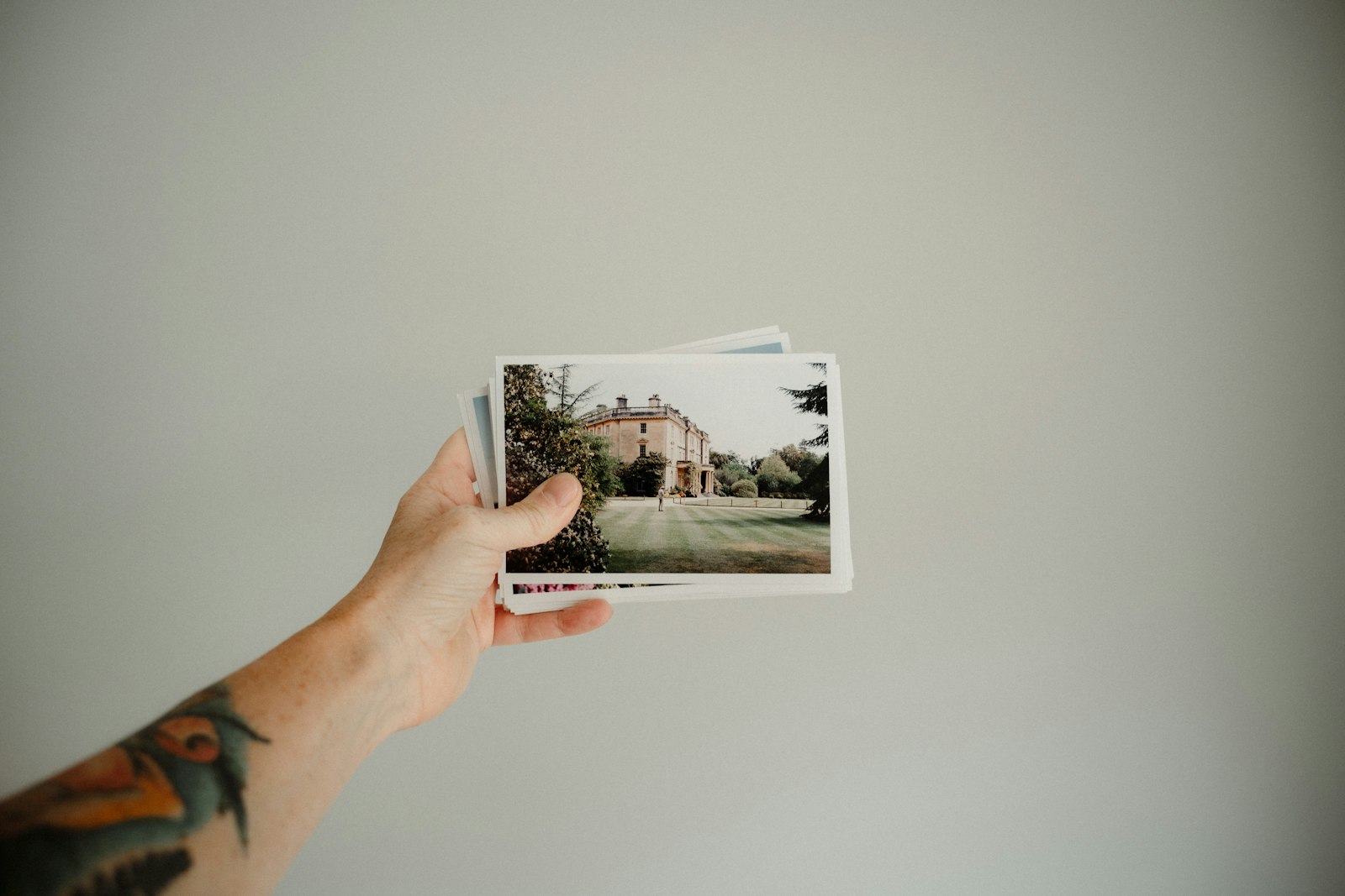 Une main tient quelques photographies imprimées devant un mur clair