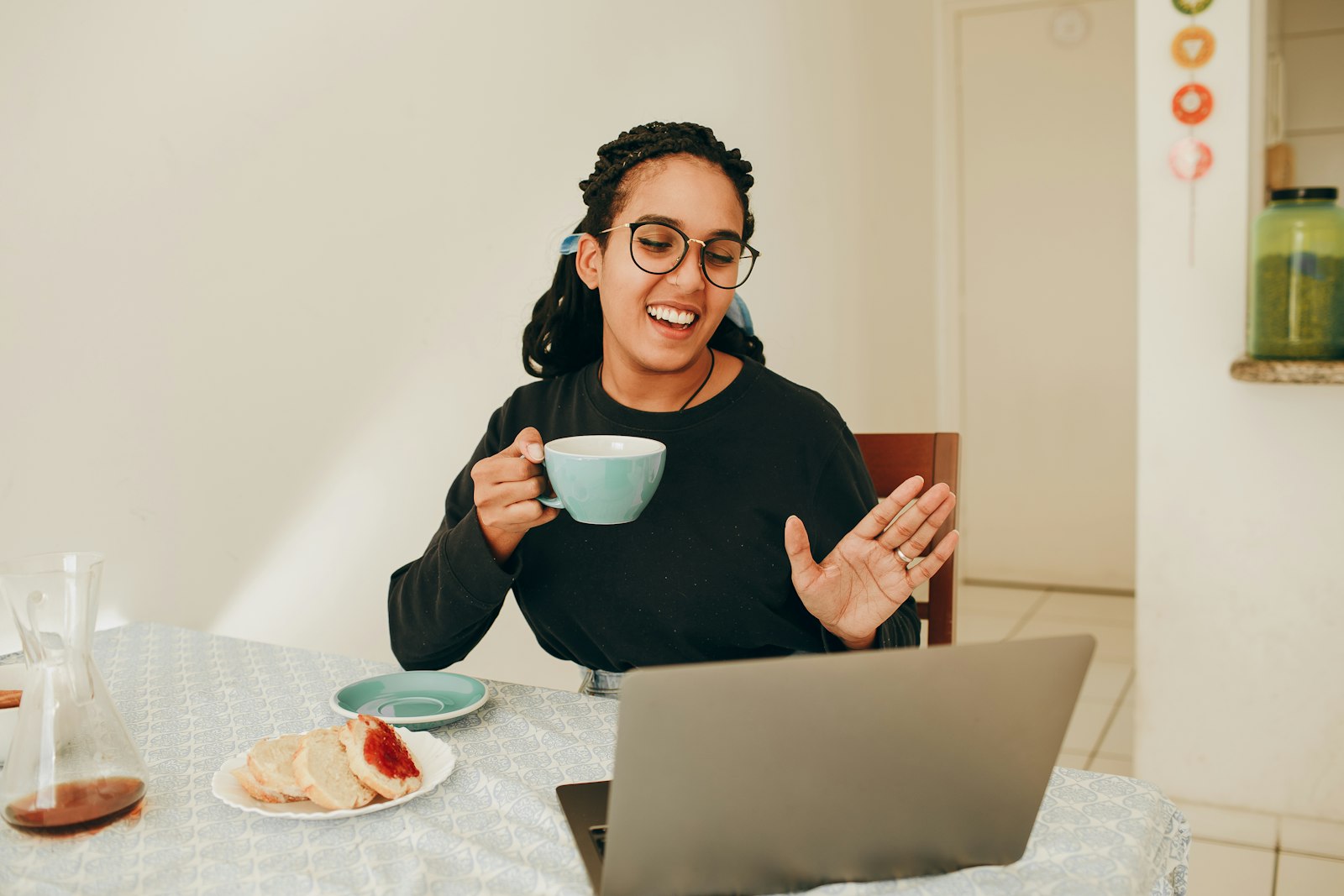 Une femme souriante, une tasse à la main, échange avec quelqu'un par visioconférence sur son ordinateur portable