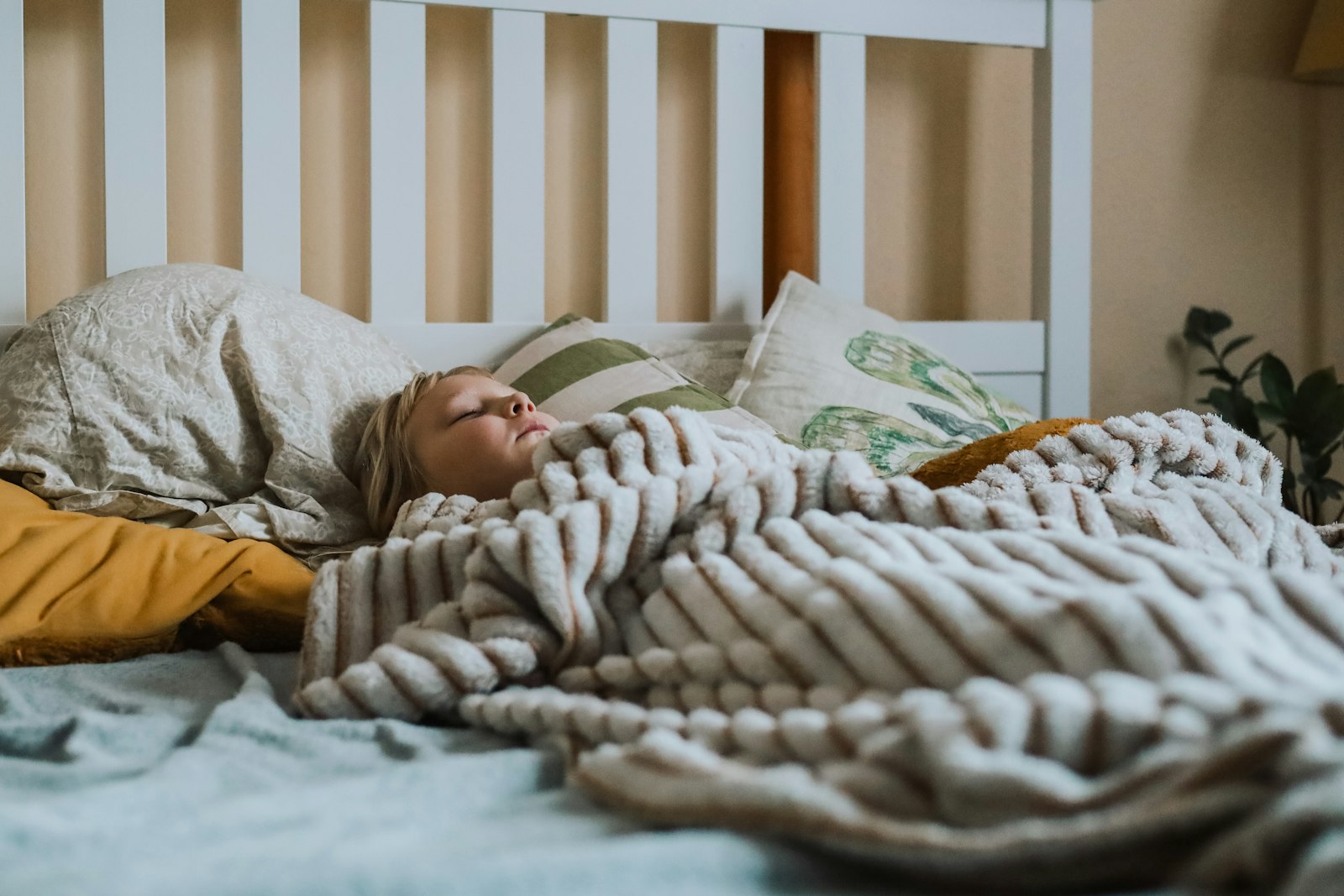Un enfant endormi paisiblement dans un lit, sous un plaid rayé