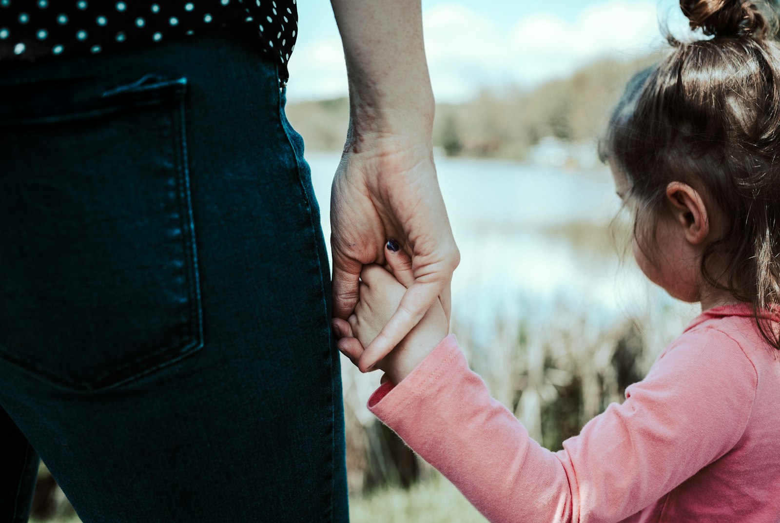 Un adulte tient la main d'une petite fille au bord d'un lac