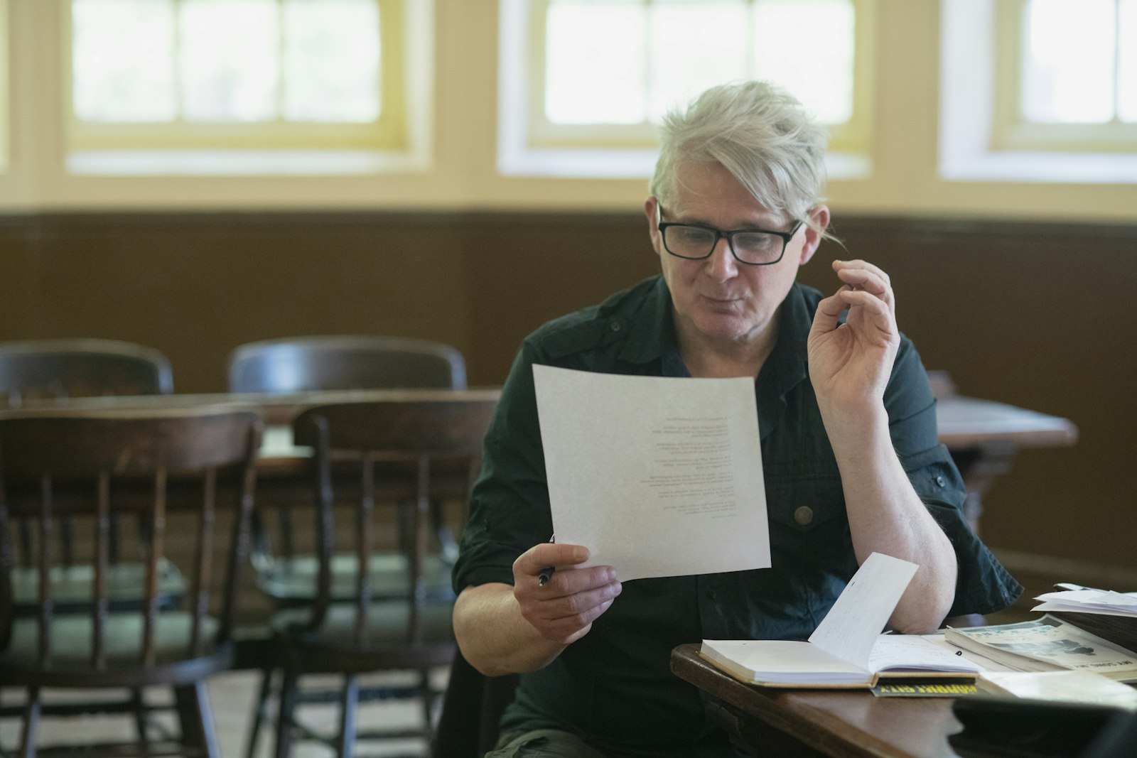 Une personne assise à une table lit attentivement une feuille, des notes ouvertes devant elle