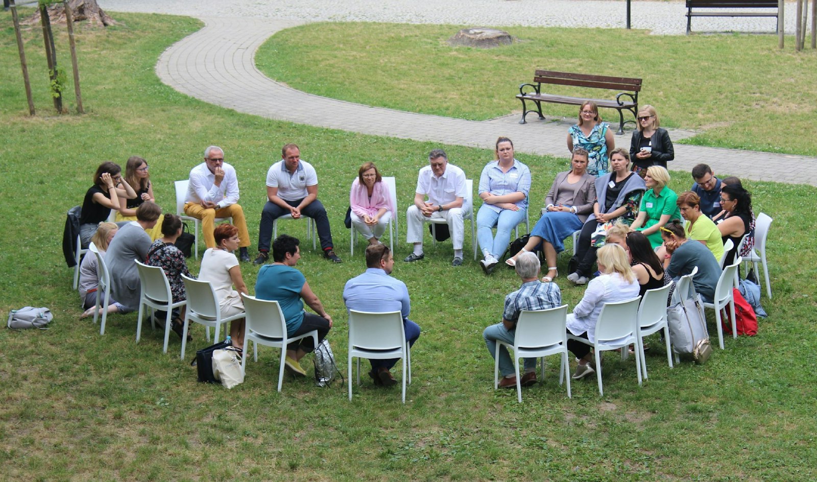 Un groupe de personnes assises en cercle sur des chaises blanches dans un jardin, en pleine conversation