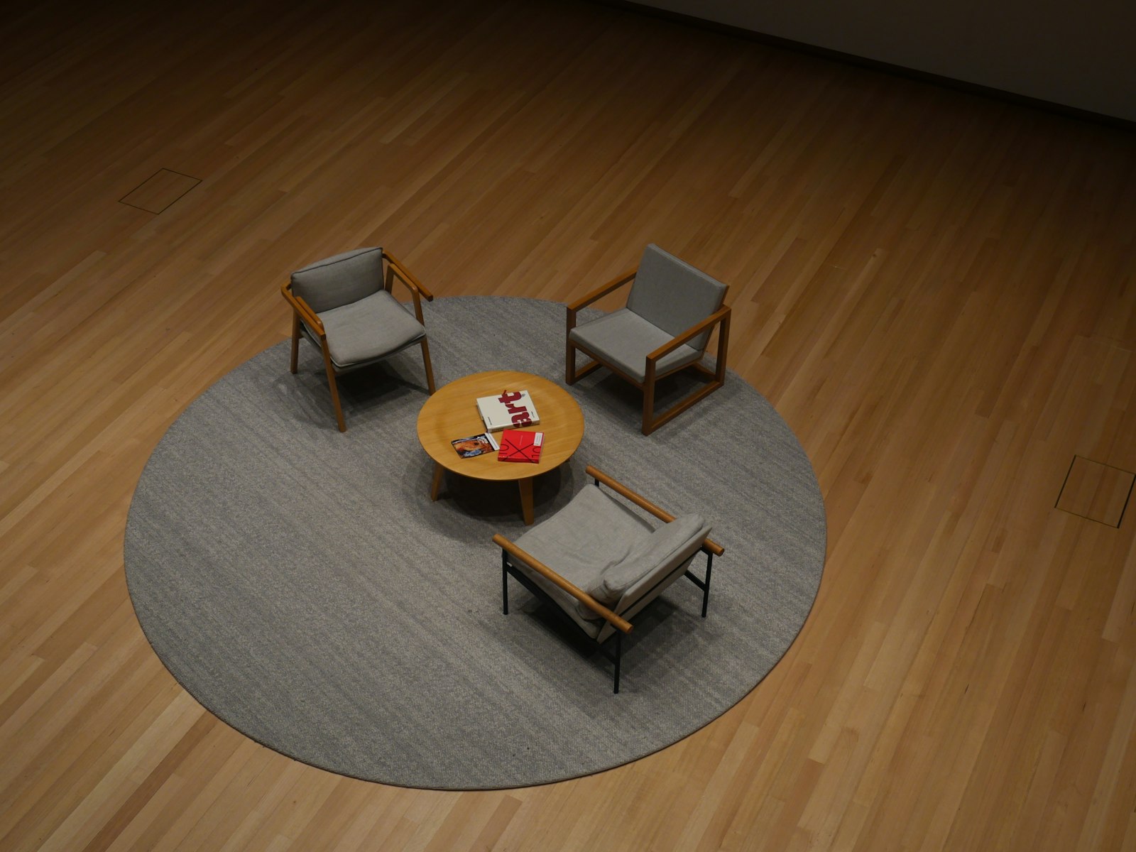 Trois fauteuils et une petite table basse disposés en cercle sur un grand tapis rond, dans une salle au parquet clair