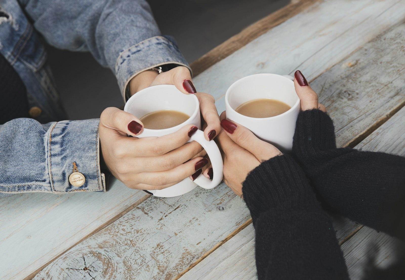 Deux personnes tiennent chacune une tasse de thé ou de café entre leurs mains, sur une table en bois clair